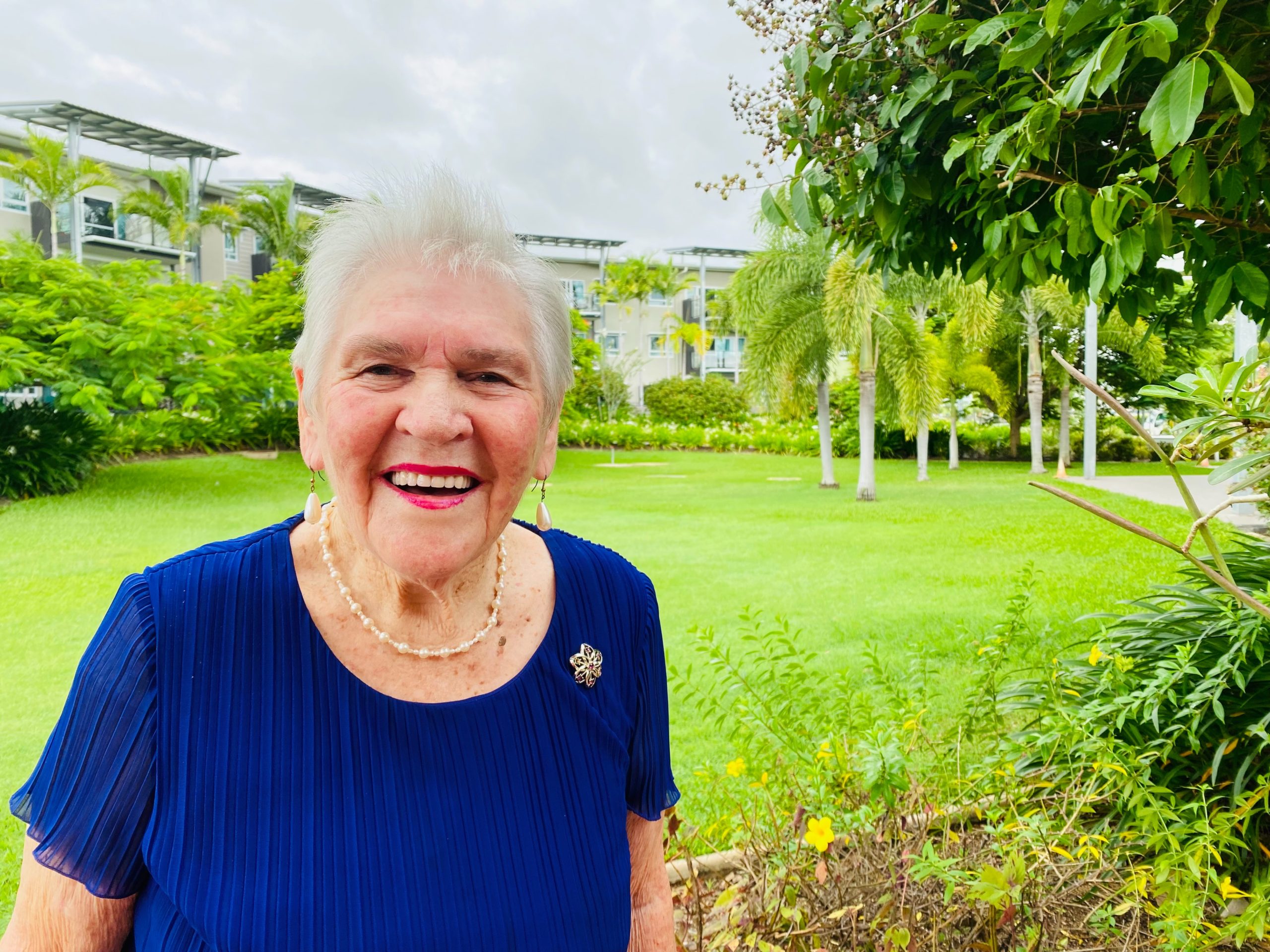 Fay, an aged care resident at Regis Kirwan, smiling and holding a crafted item in her hands, surrounded by other residents and team members