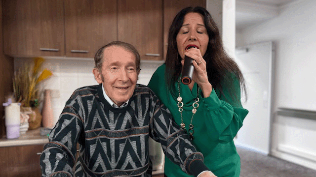 Smiling man next to woman singing into a microphone